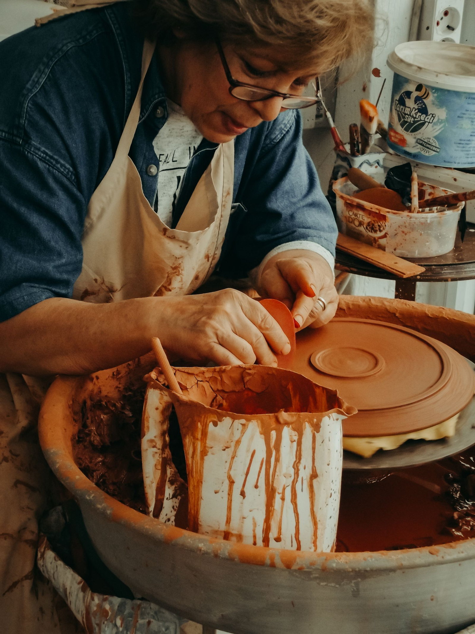 A ceramic artist shaping a clay form by hand at a workbench