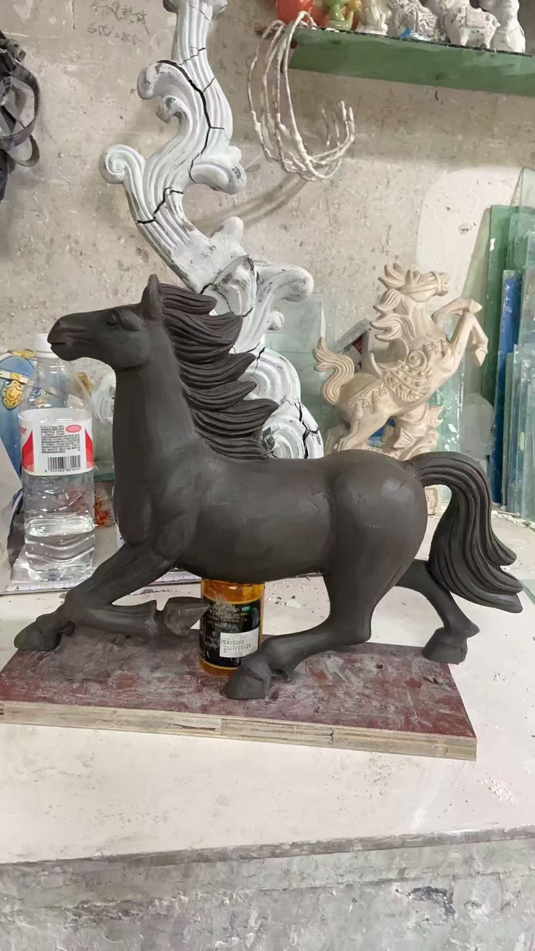 An unglazed dark clay model of a horse standing on a workbench
